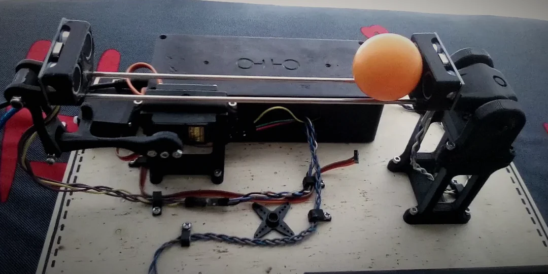 The ball and beam in 2020, with an orange ping-pong ball on its two rods beside the right-hand sensor. The servo and its arm are on the left, the box with the Arduino stands behind the rods and the pivot's stand is on the right.